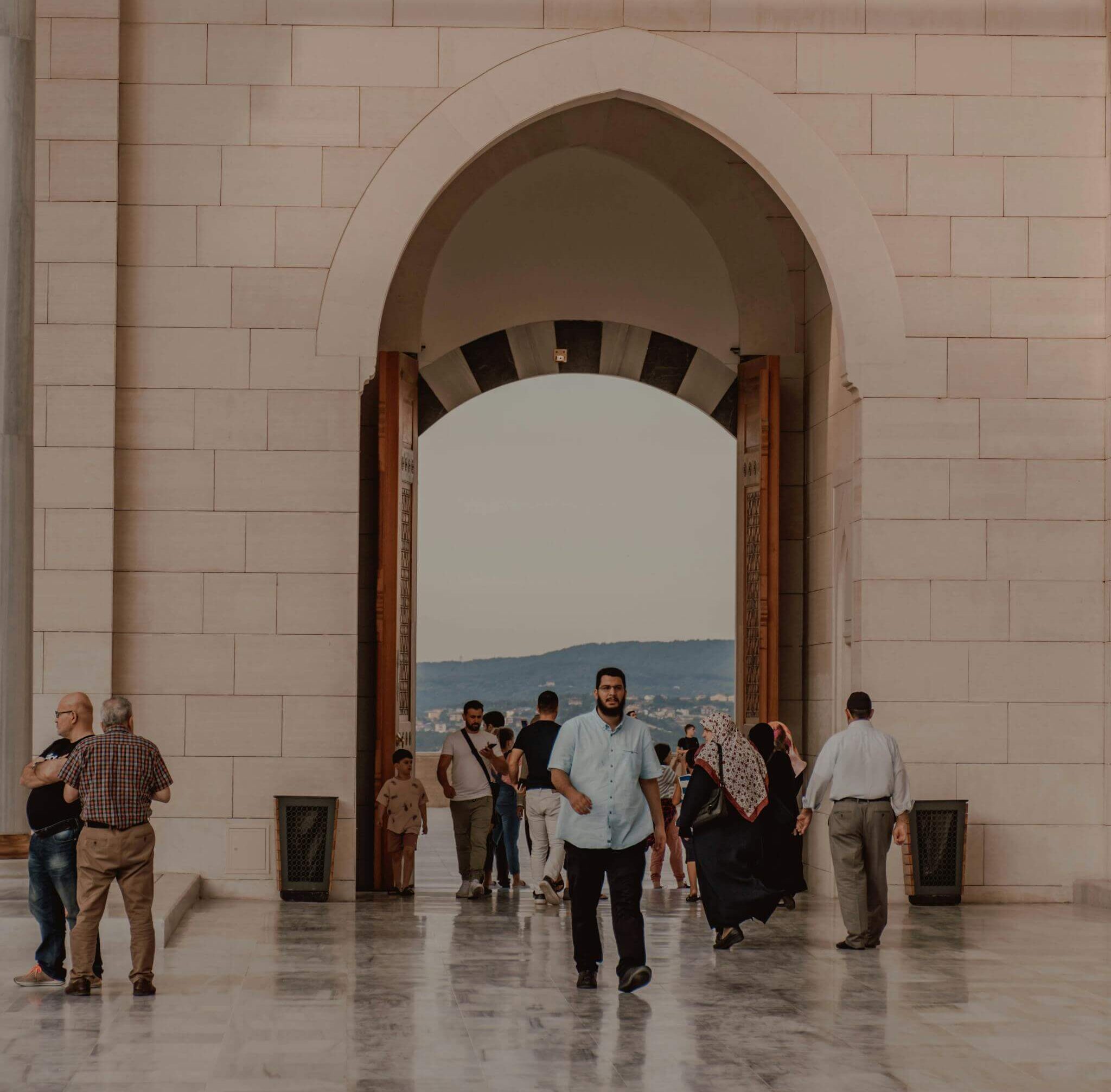 Tourists in casual clothes walking on cement floor near stone gates in Arabic decorations with picturesque view of cityscape in evening